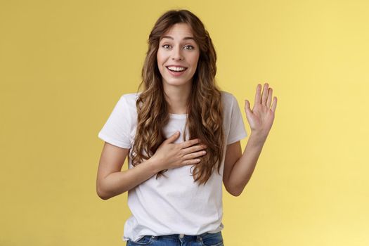 Girl introduce herself friendly joyful casual conversation smiling broadly hold hand heart raise palm waving swear tell truth be honest grinning make promise oath stand yellow background say hi