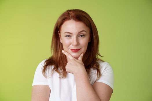 Hmm interesting choice. Intrigued cunning redhead middle-aged female hold hand face-line rub chin thoughtful smirking pleased raise eyebrow curious pondering alluring decision green background