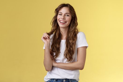 Lively joyful happy cute brunette curly long hairstyle playing curl laughing joyfully having funny amusing conversation smiling toothy white perfect smile stand yellow background relaxed
