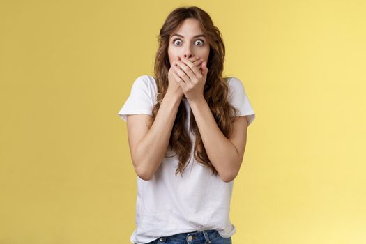 Shocked ambushed speechless cute girl hear impressive rumor shut mouth hold hands lips stare camera astonished eavesdrop juicy stunning conversation stand yellow background