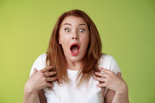 Shocked panicking redhead middle-aged woman gasping drop jaw open mouth stare camera freak-out anxious pointing herself impressed terrified frustrated nervously react green background