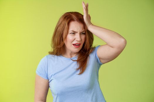Something important slip my mind. Concerned worried upset redhead mature woman punch forehead turn away frustrated frowning disappointed forget cancel appointment stand green background