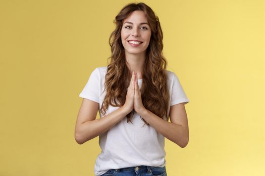 Cheerful confident outgoing young polite girl say namaste greeting asian guests smiling gladly thanking for visit hold hands pray supplication gesture asking favour begging stand yellow background