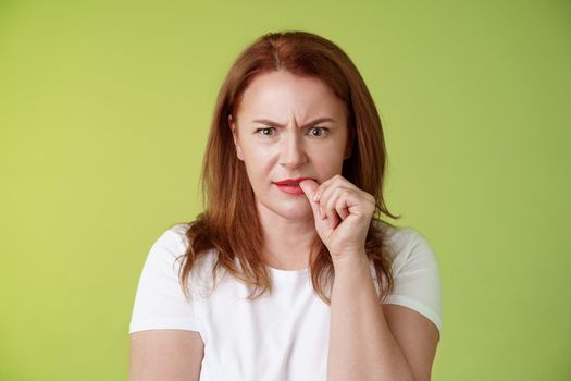 Confused puzzled redhead middle-aged mother perplexed look troubled solving troublesome situation pondering solution biting thumb nail frowning intense stare camera thinking thoughtfully