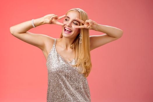 Carefree joyful beautiful fabulous blond woman having fun celebrating partying dancing happily show victory peace disco signs look aside entertained, enjoying awesome music, red background