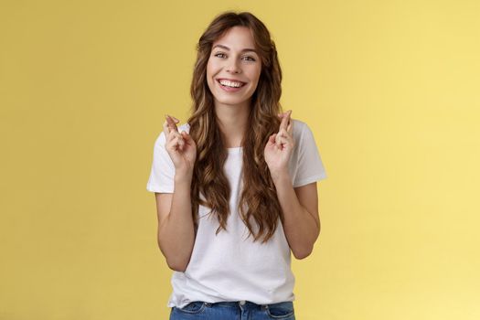 Girl faithfully believe dream come true hopefully awaiting positive results smiling broadly cross fingers good luck implore god good news stand excited optimistic yellow background