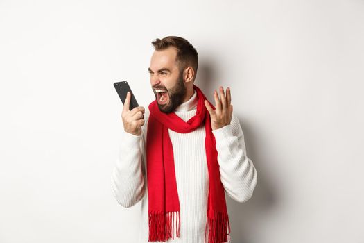 Angry man shouting at smartphone with mad face, standing furious against white background