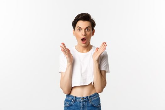 Lgbtq and pride concept. Image of surprised queer guy clap hands and looking in awe at camera, standing in crop top against white background