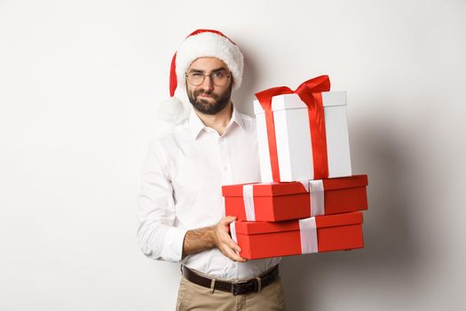 Merry christmas, holidays concept. Thoughtful man holding xmas gifts and looking suspicious at camera, celebrating New Year, white background