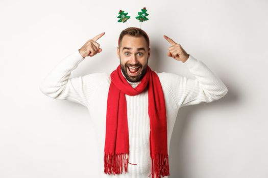 Christmas holidays. Excited man celebrating winter holidays, wearing New Year party accessory and red scarf, standing against white background