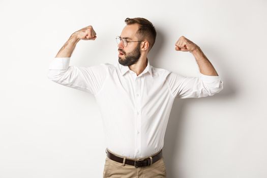 Successful businessman flex biceps, showing muscles and looking confident, feeling strong, standing over white background