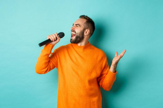 Handsome adult man perform song, singing into microphone, standing against turquoise background