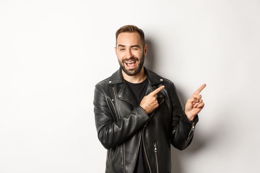 Cheeky guy in leather biker jacket, winking flirty and pointing at upper right corner copy space, white background