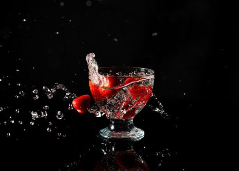 strawberries falling into a glass of water with a splash on a black background