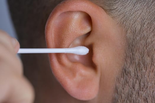 Closeup of man cleaning dirty ears with cotton swab or cotton stick