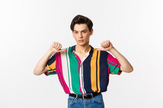 Confident and sassy gay man pointing at himself, looking self-assured, standing over white background