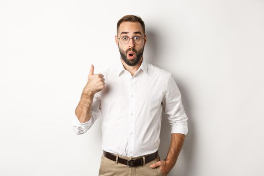 Impressed young male entrepreneur showing thumbs-up, praise something good, like and agree, white background
