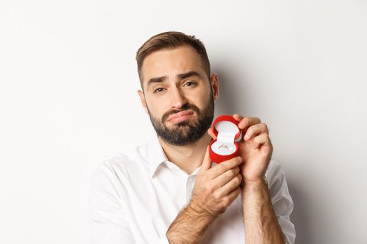 Close-up of hopeful man begging to marry him, looking sad and showing wedding ring, making a proposal, white background