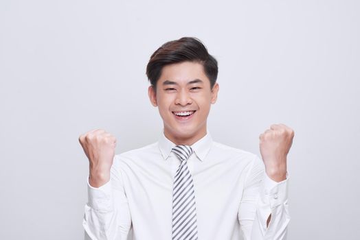 Portrait of victorious man looking up while standing on white background and celebrating with fists in the air