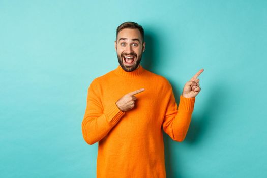 Excited man making an announcement, pointing fingers right your logo, standing over turquoise background