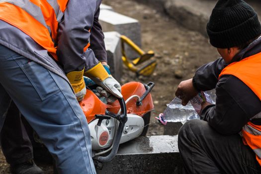 Back view of workers wearing reflective vest cutting and repairing street curbs in Bucharest, Romania, 2020
