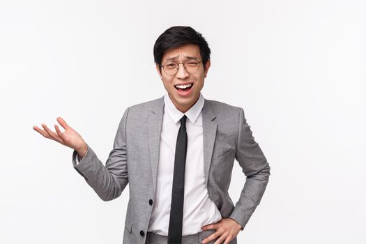 Waist-up portrait of skeptical and frustrated asian young businessman in suit, pointing at something with judgement or dismay, discuss bad project, scolding employee, white background