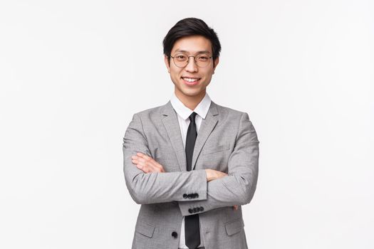 Waist-up portrait of confident smart and talented asian businessman, successful employer in grey suit, start own enterprise, earn money, cross hands over chest assertive smiling, white background