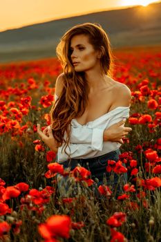 Beautiful young long haired woman in a poppy field at sunset with flying hair. Dressed in a white shirt and denim skirt.