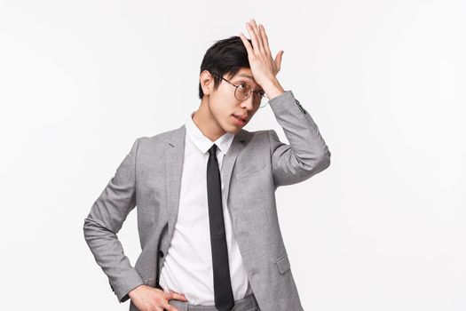 Waist-up portrait of handsome forgetful asian male employer, office manager forgot buy something, punch forehead and looking away sighing, remember important task, white background
