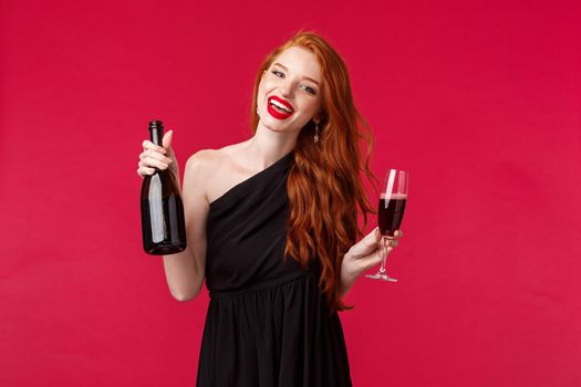 Portrait of carefree gorgeous redhead woman partying with friends, drinking from glass, holding bottle champagne and dancing during bachelorette night, smiling camera wear black dress