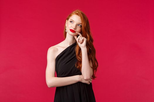 Fashion, luxury and beauty concept. Portrait of dreamy elegant and sensual young redhead woman with red lipstick, evening makeup, wear luxurious black dress, look up as dreaming or imaging
