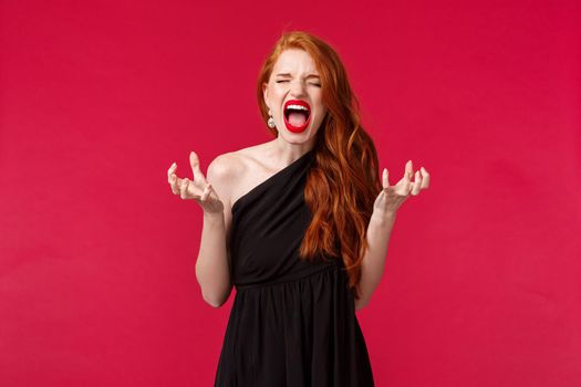 Depressed and upset redhead caucasian woman in black dress complaining someone ruined her party, screaming and shouting with closed eyes, shaking head displeased, black background