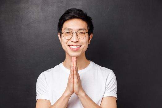 Close-up portrait of friendly, polite and relaxed young asian man with happy smile, hold hands in pray, palms pressed together over chest, smiling at camera, say namaste, praying