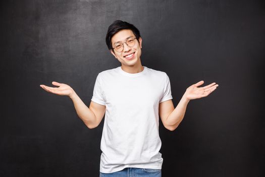 No big dea. Handsome carefree and unbothered asian guy shrugging and spread hands sideways clueless, have no idea, dont know anything and not care at all, black background, smiling
