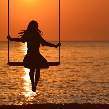 Silhouette of child girl on swing in sunset at seaside