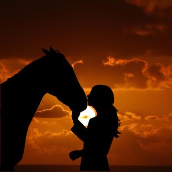 Silhouette of a young girl with horse giving him a kiss at the sunrise