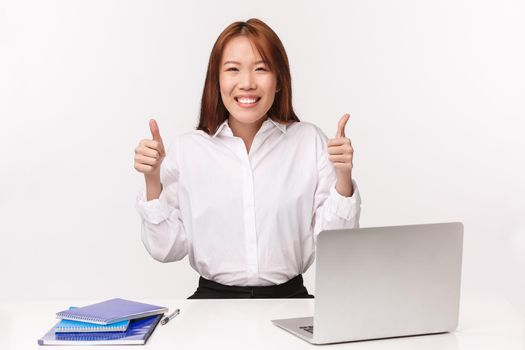 Career, work and women entrepreneurs concept. Close-up portrait of cheerful young assured asian office lady approve idea, guarantee quality of service, sit at desk with laptop and documents