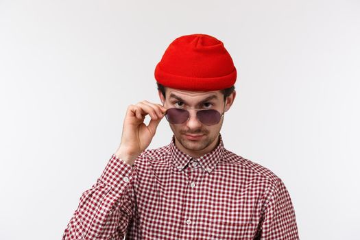 Skeptical and doubtful handsome hipster young man with moustache, red beanie, look from under forehead with disbelief, take-off glasses to make serious judgemental gaze at strange person