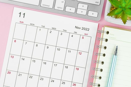 November 2022 calendar sheet with keyboard computer on pink background.