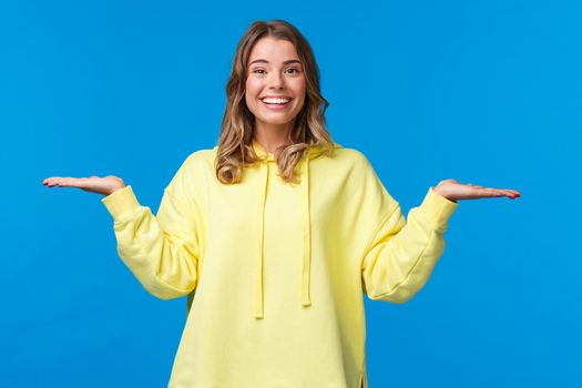 Carefree happy smiling woman weighing something in arms, as if holding two products, look camera suggest make choice, deciding between variants, stand blue background