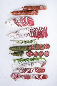 Variety of dry cured fuet and chorizosalami sausages, whole and sliced on white textured background, topview