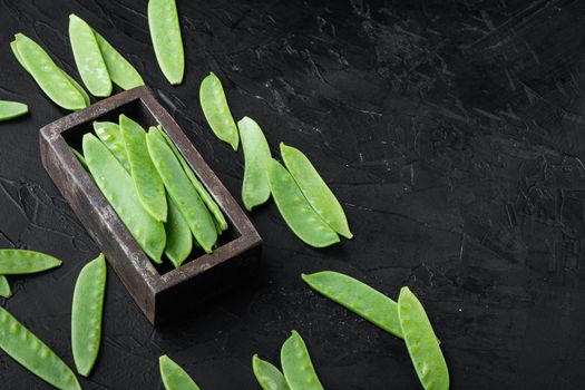 Sugar snap peas, raw ripe baby pods, in wooden box, on black stone background , with copyspace and space for text