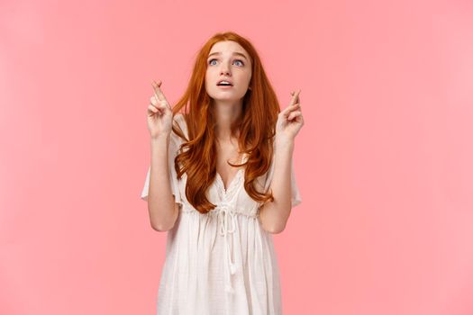 Hopeful and excited, dreamy cute redhead girl making wish on shooting star, looking up amused and overwhelmed, cross fingers good luck, waiting with aspiration for dream come true