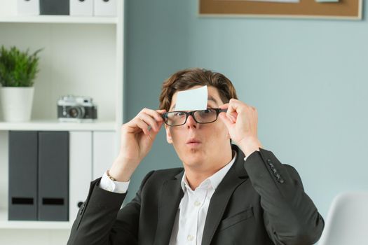 Business people, joke and fool concept - portrait of young man with glasses and shirt with blue sheet glued to his forehead.