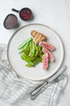 Grilled Ahi Tuna Steak with spring onions and sugar snap peas, on plate, on white stone background, top view flat lay