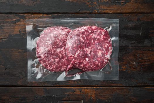 Beef patties in a vacuum packing, on old dark wooden table background, top view flat lay