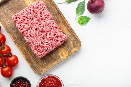 Ingredients for cooking Bolognese sauce, minced beef meat tomatoe and herbs, on wooden tray, on white stone background, top view, flat lay, with copy space for text