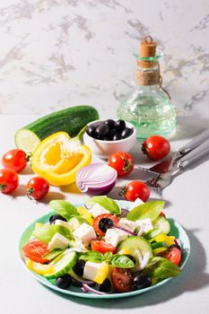 Fresh homemade greek salad with basil leaves on a plate and ingredients for cooking on the table. Domestic life. Vertical view. Hard light
