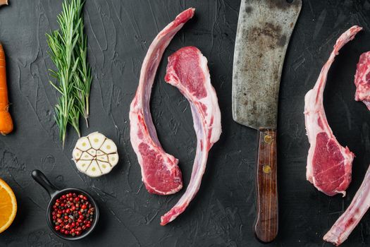 Raw lamb chops or mutton cuts, with ingredients carrot orange, herbs, on black stone background, top view flat lay