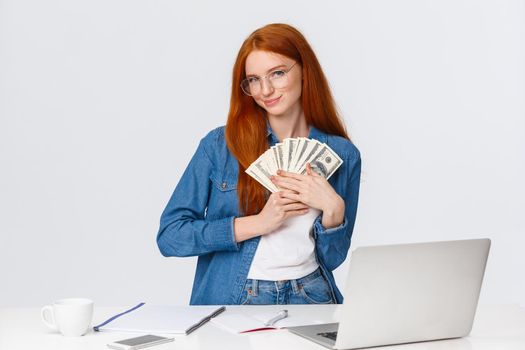 Girl loves money, feeling warmth of cash in hands, standing silly and delighted, received paycheck and grinning, going shopping online, making internet order, standing near laptop, white background